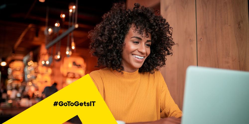 Woman working remotely in a café protected from remote work security risk by IT’s best practices.