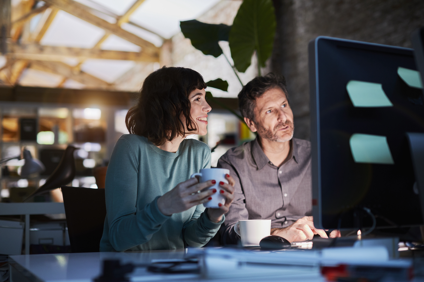 Young woman and man looking at an office desktop monitor leveraging background access vs unattended access to provide remote monitoring and management support