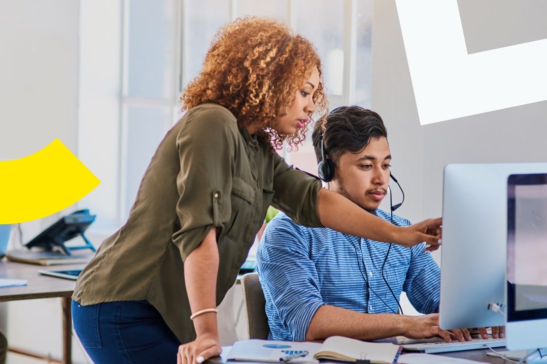 Gerente treinando agentes no software de gestão de qualidade com IA, com o pessoal usando fones de ouvido e trabalhando em sua estação de trabalho.